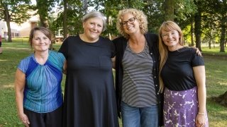Four faculty and staff members gather for a group photo in a bright wooded area on campus.