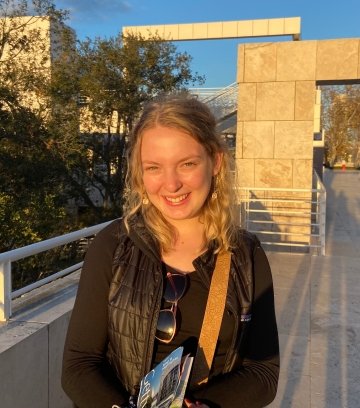 Abbie Cooper, class of twenty-twenty-two, wearing a black shirt and vest and standing in the sunshine.