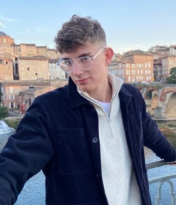 Rowan Travis, class of twenty-twenty-two, standing on a bridge overlooking a small city behind him.