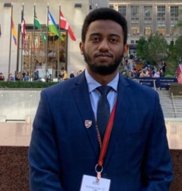 Zemichael Habtegiorgis, class of twenty-twenty-two, wearing a navy blue blazer and standing outside Rockefeller Plaza in New York City.